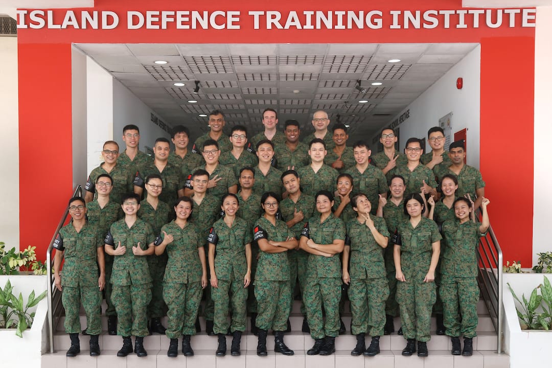 A group of soldiers in green military uniforms standing in front of a building marked "Island Defence Training Institute."